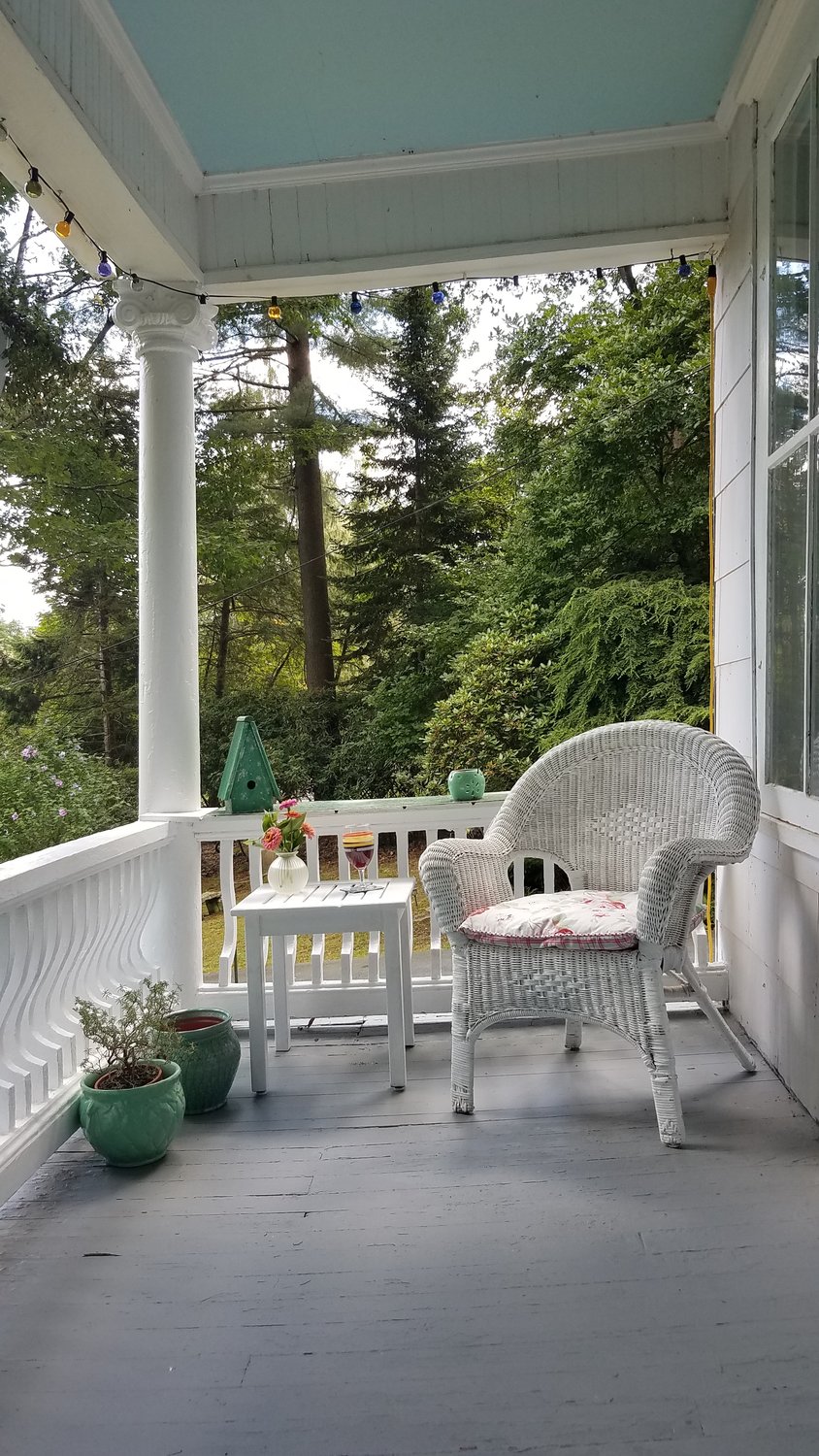This comfortable porch, complete with an antique wicker chair, is the perfect place for catching a cool summer breeze. Because of the lush green wooded area that surrounds the house, there is a delightful sense of the outdoors within the confines of the porch. Against the white background, simple accents of greens and blues enhance the porch’s 19th-century Victorian architectural elements. ..